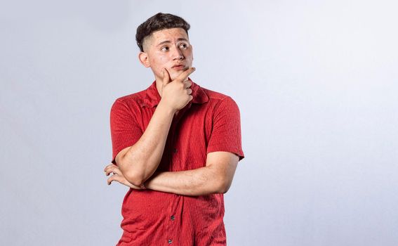 young man wondering with his hand on his chin on an isolated background, a guy thinking with his hand on his chin.