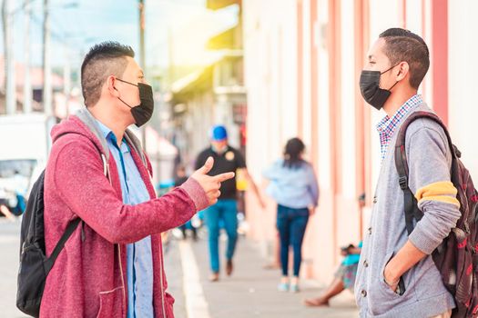 Two young people with mask having a conversation outdoors, two friends with face mask having a conversation, concept of conversation and social distance