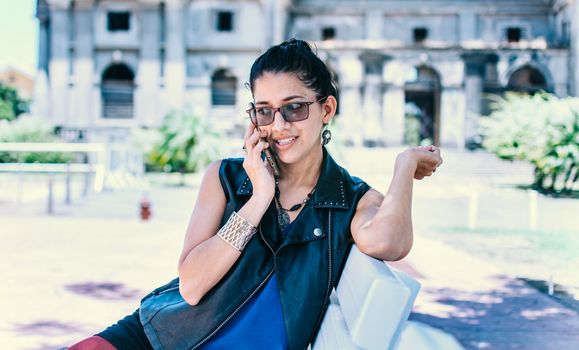 Urban style girl sitting on a bench calling on the phone, An attractive girl sitting talking on the cell phone, Girl sitting in a park calling on the phone