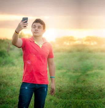 Young man taking a picture, young man taking selfie in the field, young man in the field taking a picture