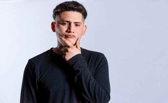 young man wondering with his hand on his chin on an isolated background, a guy thinking with his hand on his chin.