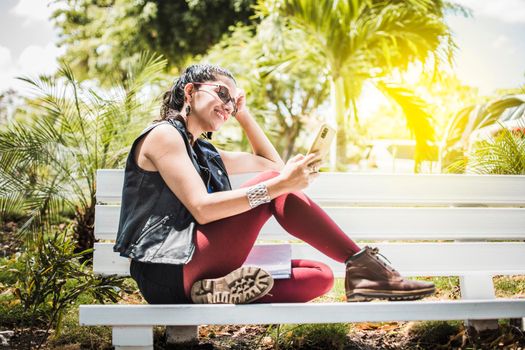 Girl sitting on a bench checking her cell phone, Happy woman sitting in a park texting on her cell phone, Happy woman sitting on a bench sending a text message