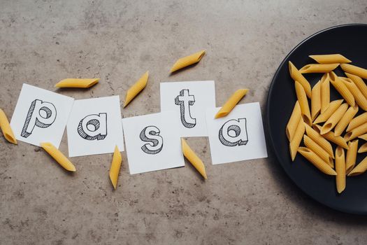 Lettering with Handful of Pasta Laid Up on the Black Plate on Table