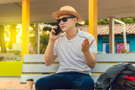 An attractive guy calling on a cell phone on a bench, a man sitting on a bench calling on the phone.