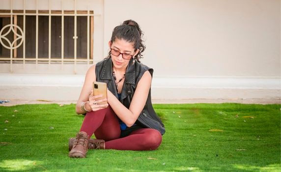 Girl sitting on the grass checking her cell phone, urban girl sitting with her cell phone, Lifestyle of woman with cell phone