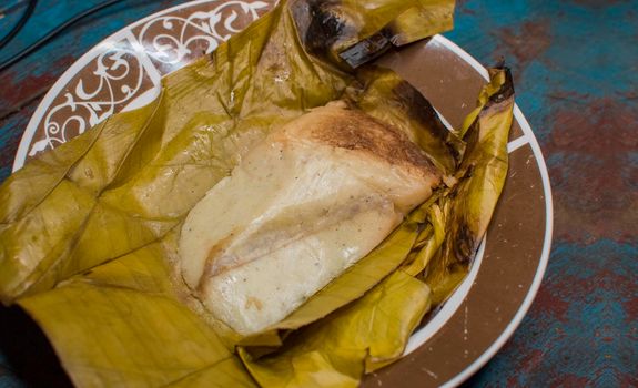 Stuffed tamale served on wooden table, stuffed tamale on banana leaf served on wooden table, typical nicaragua food