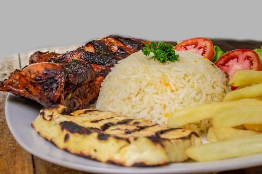 Pork rib with rice, fried cheese and tomato salad, Nicaraguan food served on wooden background, Plate of pork rib and rice served on wooden background