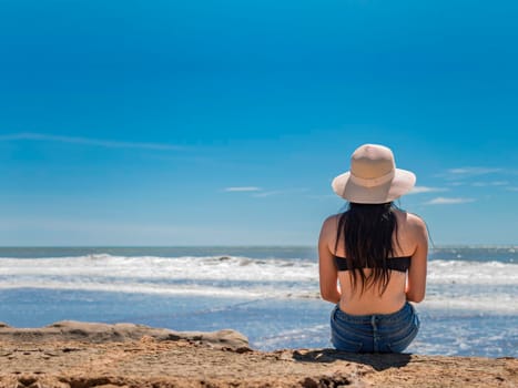 woman in hat from back to the sea, girl in hat looking to the sea, vacation concept, rear view of a girl watching the sea