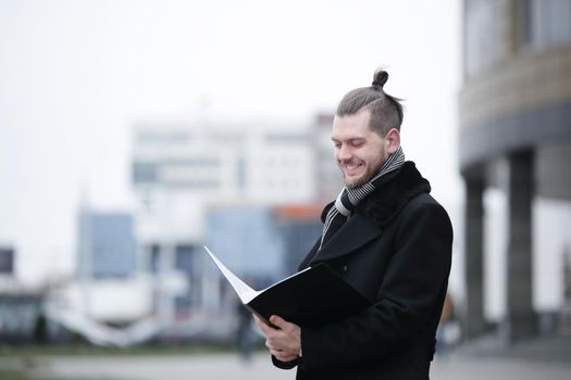 confident businessman reading documents standing on a city street.