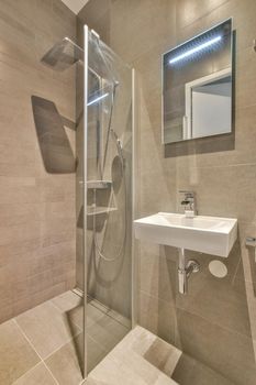 Shower faucets attached to tiled wall near glass partition and ornamental curtail in washroom at home