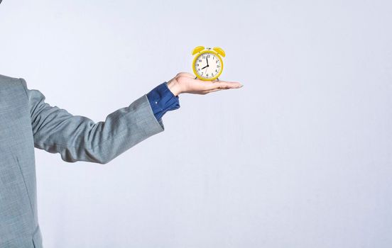 A hand holding a table clock on isolated background, close up of a hand holding an alarm clock, businessman hand holding clock isolated