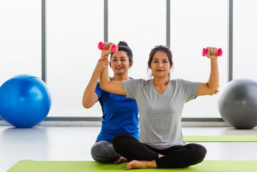 Asian young woman teacher teach adult student doing yoga hands holding dumbbells training body in studio. Two woman exercise workout with dumbbells, female sport fit workout concept