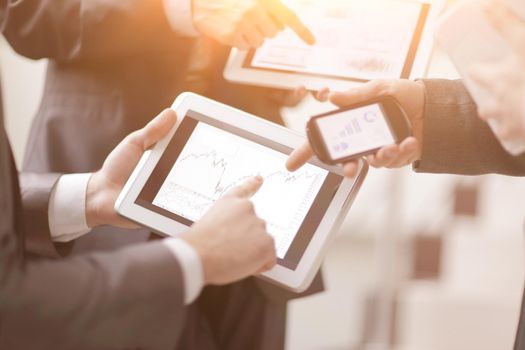 Businessmen at meeting presenting charts on smartphone, tablet.