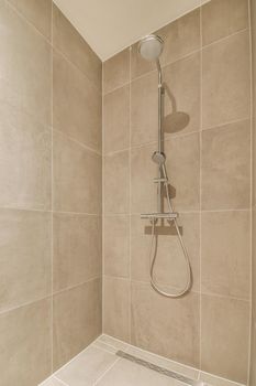 Shower faucets attached to tiled wall near glass partition and ornamental curtail in washroom at home