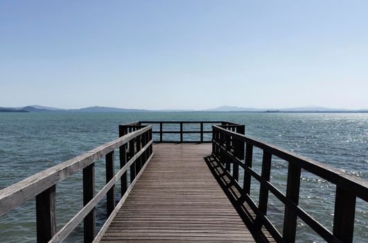 Long wooden pier on lake  Trasimeno , Italy , in the background coastline