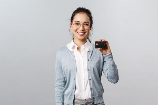 Technology, online purchases and finance concept. Pleasant good-looking asian woman in glasses, using credit card to pay without cash, making payment in internet, shop at home.