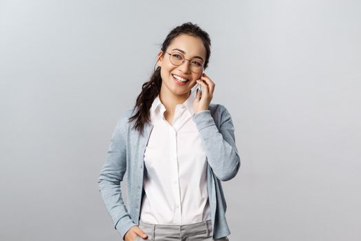 Office lifestyle, business and people concept. Friendly asian female in glasses, white collar shirt, laughing and looking away casually talking on phone, have conversation use mobile connection.