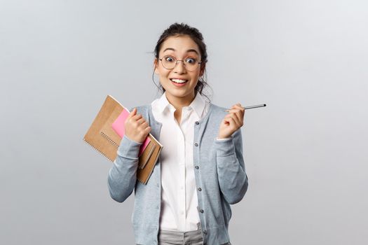 Education, teachers, university and schools concept. Enthusiastic, amused asian female in glasses, student gesturing with pencil in hands, holding notebooks, talking to classmate at campus hall.