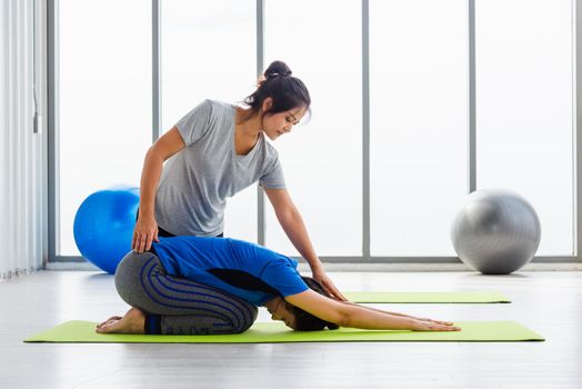 Asian young woman teacher teach adult student doing yoga stretching position in studio. Two woman teaching yoga and fun together, female sport fit workout concept