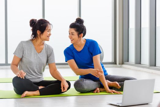 Overhead two Asian lifestyle adult and young woman in sportswear sitting floor on mat look laptop computer for training videos online in yoga studio, fit sport healthy workout exercise