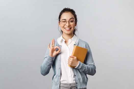 Education, teachers, university and schools concept. Her schedule is under control. Portrait of satisfied smiling asian woman, wink encourage all good, show guarantee okay sign pleased.