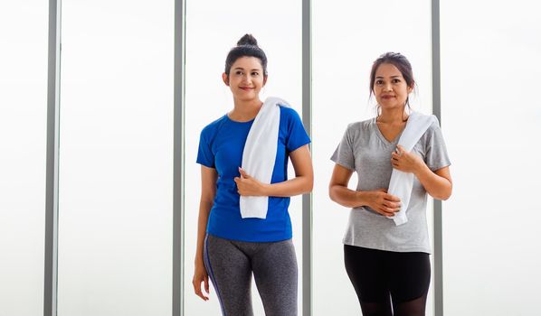 Asian adult and young woman smiling with towel around neck after yoga and exercise. Portrait of happy beautiful female standing indoor yoga studio, sport healthy workout concept