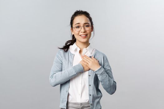 Portrait of touched, flattered young woman, teacher or office worker in glasses, hold hands on heart impressed with ncie gesture of coworker, smiling and sighing, look thankful and pleased.