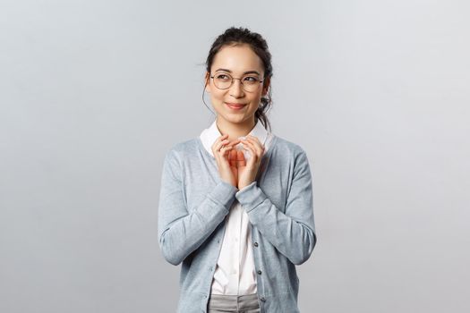 Lifestyle, people and emotions concept. Cute and smart asian woman feel like genius, have great plan, steeple fingers look away thoughtful, imaging something good, stand grey background.