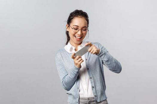 Technology, online and mobile lifestyle concept. Enthusiastic, happy smiling asian woman holding smartphone both hands and tilt phone to pass level, playing racing game amused.