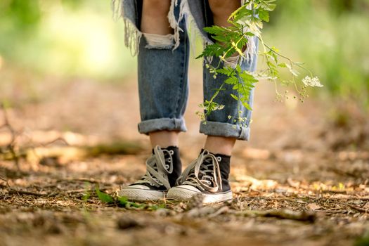 Girl legs in jeans denim and sneakers in field with flowers closeup details. Female person in cotton pants and black keds at nature