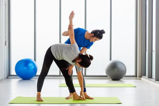 Asian young woman teacher teach adult student doing yoga stretching position in studio. Two woman teaching yoga and fun together, female sport fit workout concept