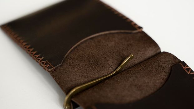Open brown men's money clip handmade leather wallet. Empty money clip wallet with a two pockets for cards lies on a white table. Selective focus, copy space