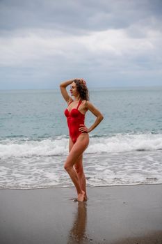 A beautiful and sexy brunette in a red swimsuit on a pebble beach, Running along the shore in the foam of the waves.