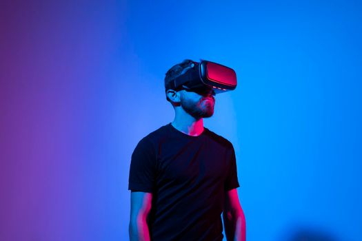 Young bearded man in virtual reality helmet plays online game in metaverse. Game simulates behavior in fictional world, gadgets and virtual reality addiction. Future technology concept
