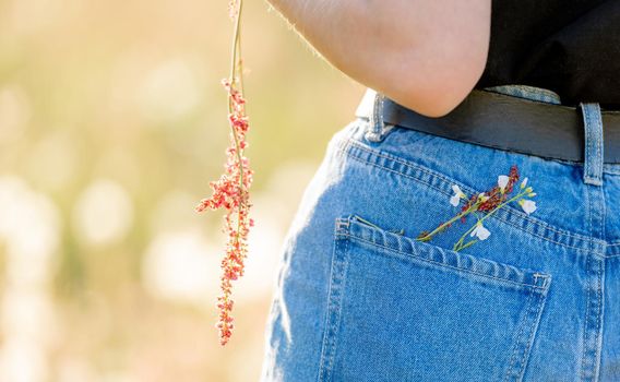 Girl wearing jeans denim with flowers closeup details. Female person in cotton pants in field