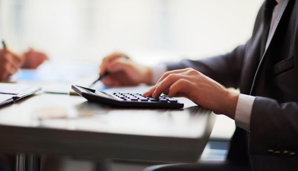 Business people counting on calculator sitting at the table. Close up of hands and stationery