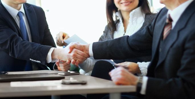 Mature businessman shaking hands to seal a deal with his partner and colleagues in a modern office