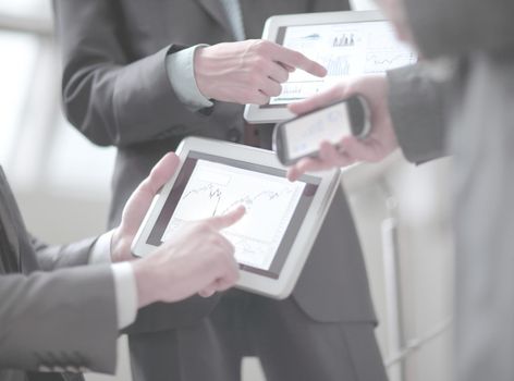 Businessmen at meeting presenting charts on smartphone, tablet.