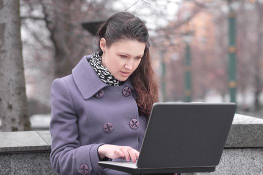 young woman uses laptop sitting on bench in city Park.