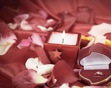 candle and a diamond ring on a background of rose petals . photo with copy space