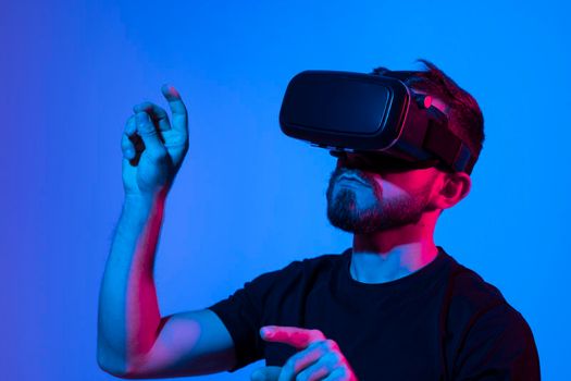 Man in virtual 3d glasses working on a project in a studio in neon light. Man playing video games with a friends at home using vr goggles