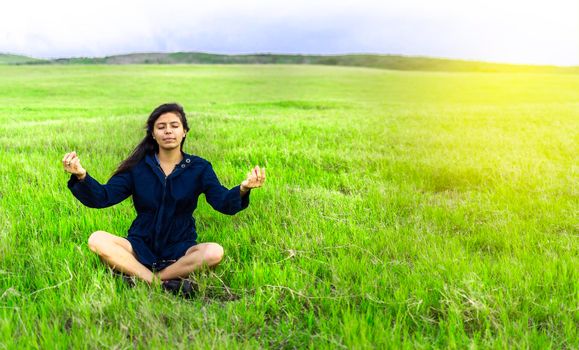 Woman in the field sitting meditating, woman doing yoga in the cool field