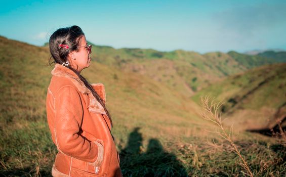 Girl in the field looking at the horizon, woman in jacket with glasses on a hill