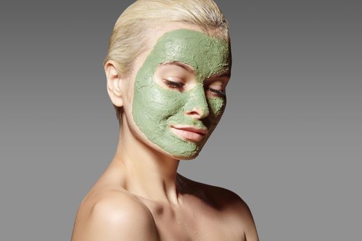 Beautiful Woman Applying Green Facial Mask. Beauty Treatments. Close-up Portrait of Spa Girl Apply Clay Facial mask on grey background.