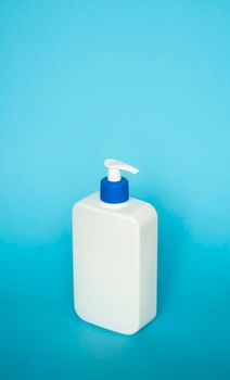 Large white plastic bottle with pump dispenser as a liquid container for gel, lotion, cream, shampoo, bath foam on blue background