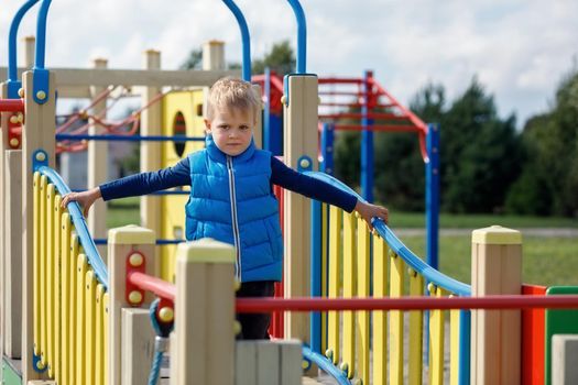A cute, blond child walks in the modern colorful outdoor playground.