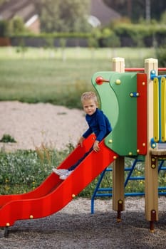 The cute kid slides on the colorful modern outdoor playground slide.