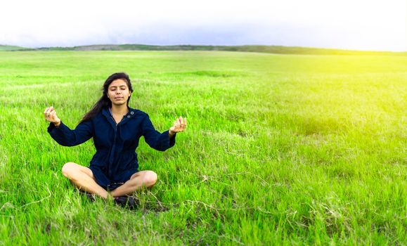 Woman in the field sitting meditating, woman doing yoga in the cool field