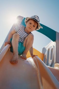 The little boy in a sunny day at the top of the slider he not dare to slip down