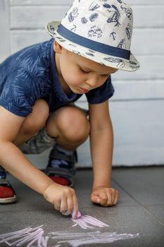 A boy draws with crayons on the asphalt . Painting. Summer games on the street. Childrens entertainment and leisure. Child puts a lot of effort and learns.